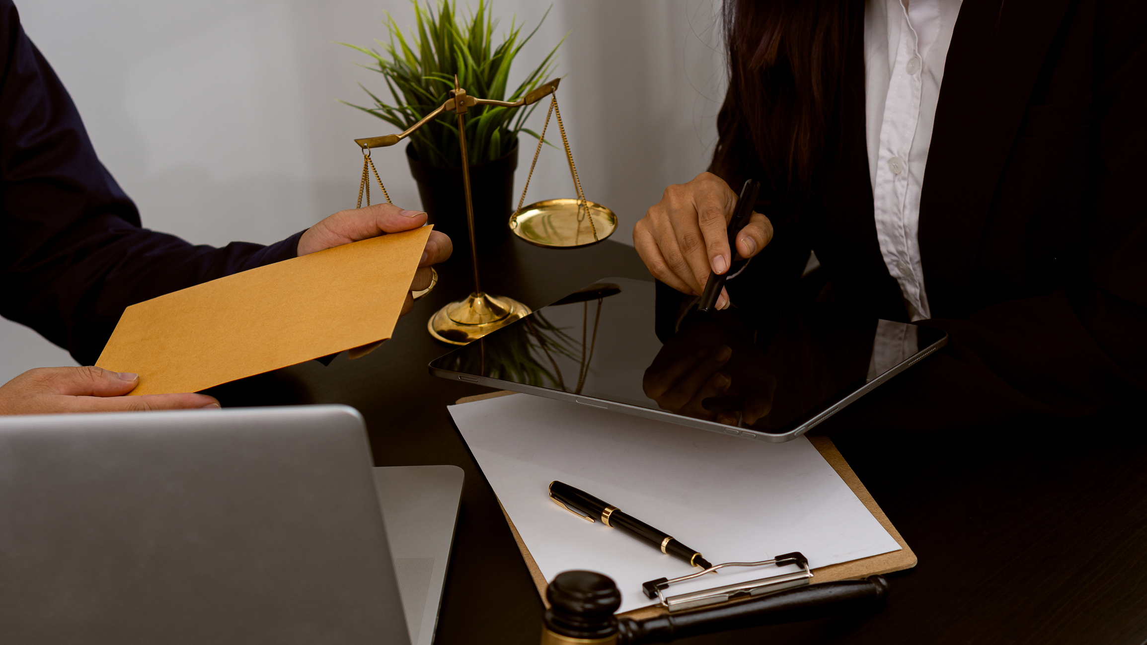 Businessman offers money to lawyer in office with laptop and scales of justice.